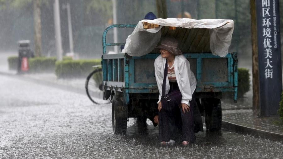 17.jun.2015 - Pedestre se protege de chuva forte sob carga de veículo em Pequim, na China