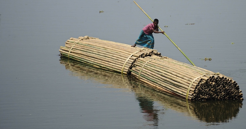 Jovem conduz pilhas de bambus ao longo de uma via navegável em Dhaka