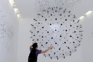Instalação da artista alemã Karina Smigla-Bobinski permite que o visitante interaja com um globo transparente que flutua pela sala. O globo é coberto por pontas de giz preto, que desenham as paredes brancas da sala - Divulgação