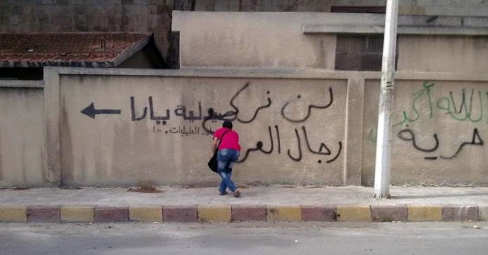 Homem picha frases anti-regime em muro na cidade de Hama, na Síria, nesta segunda-feira (30)