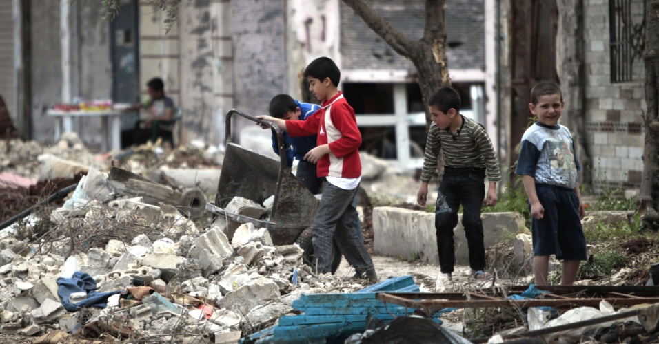 Crianças sírias removem destroços da entrada de suas casas no bairro de Bab Amro, na periferia de Homs