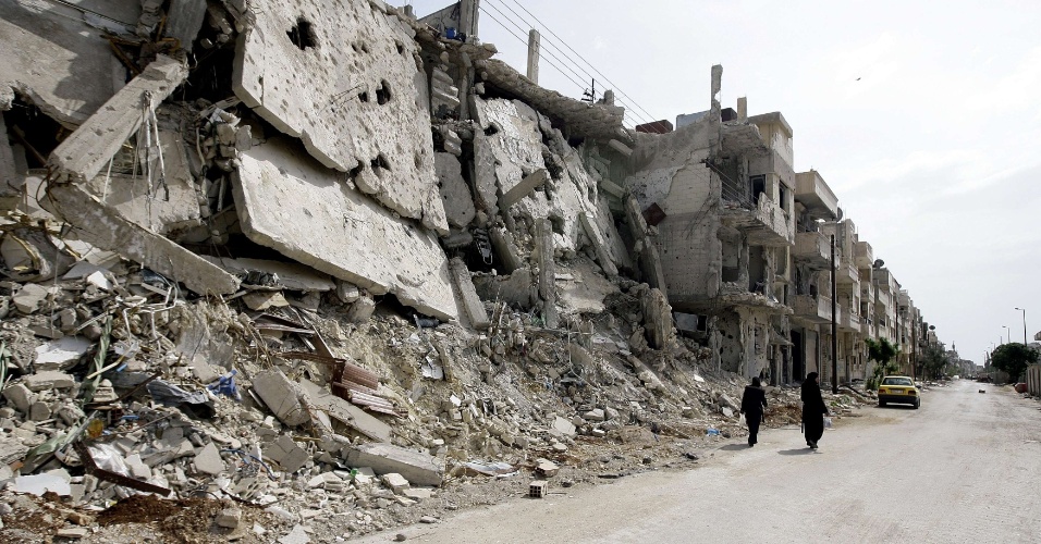 Mulheres sírias caminham ao lado de edifícios destruídos no bairro de Bab Amro, na periferia de Homs