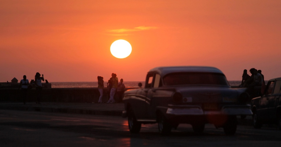 7.mai.2012 - Pessoas assistem ao pôr do sol com um táxi licenciado passando na avenida "El Malecon", à beira-mar de Havana, em Cuba