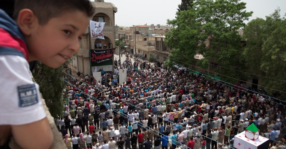 11.mai.2012 - Garoto sírio observa muçulmanos durante as orações tradicionais das sextas-feiras em Qusayr, a 15 km de Homs