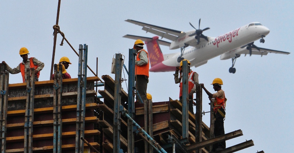 14.mai.2012 - Trabalhadores da construção civil em andaimes em uma futura estação de metro, com um avião SpiceJet Airlines voando  na cidade de Chennai