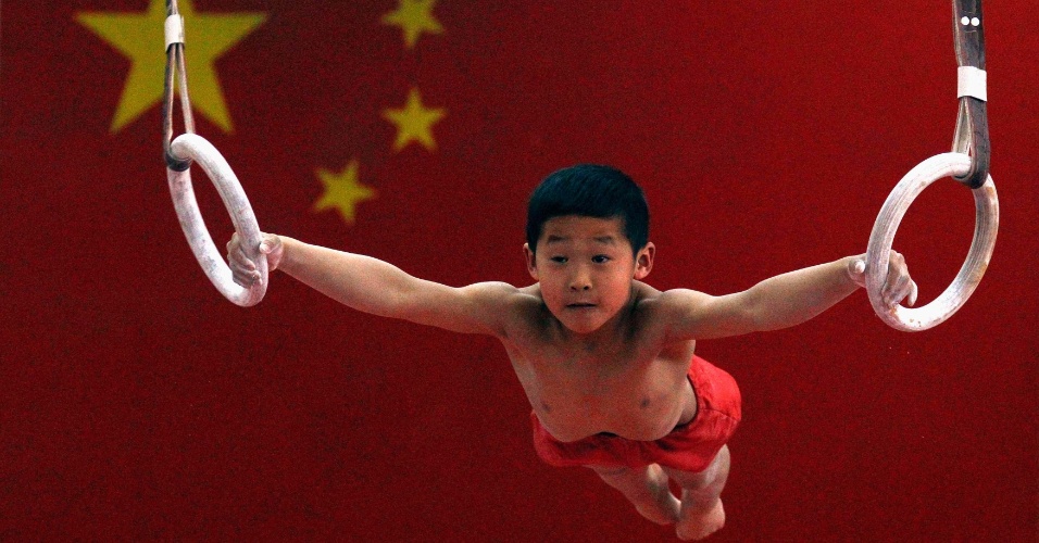 14.mai.2012 - Um jovem ginasta pendurado nas argolas em frente de uma bandeira nacional chinesa durante uma aula de ginástica para crianças entre sete e dez anos na Escola de Esportes Shichahai em Pequim