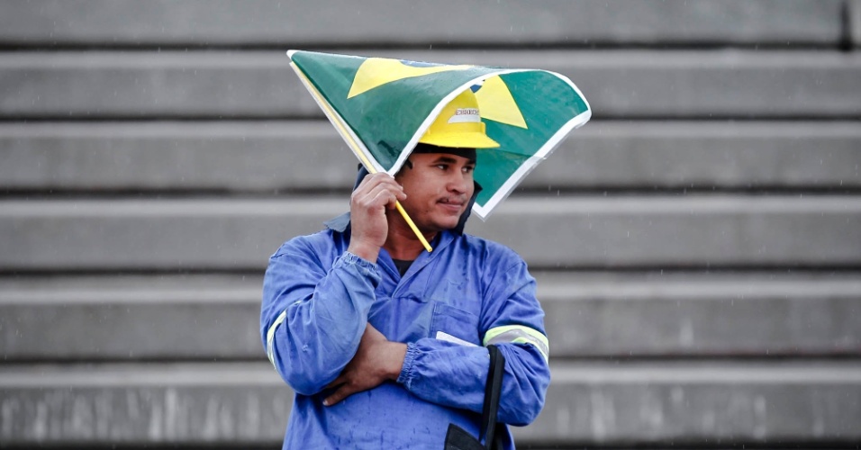 Operário usa bandeira do Brasil para se proteger da garoa em evento do Tribunal Superior do Trabalho no Itaquerão