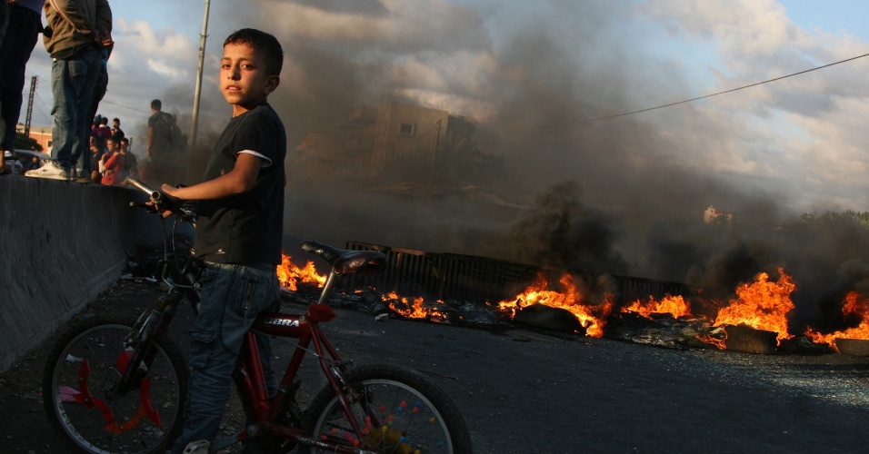 21.mai.2012 - Um garoto para em frente à barreira de fogo acesa por moradores sunitas da cidade de al-Abdeh com o objetivo de bloquear a estrada após o funeral do xeique Ahmad Abdel Wahed