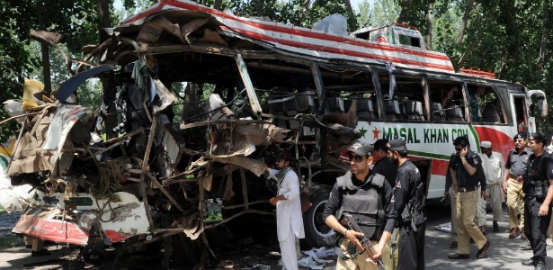 Agentes de segurança examinam destroços de ônibus destruído após explosão de bomba no Paquistão