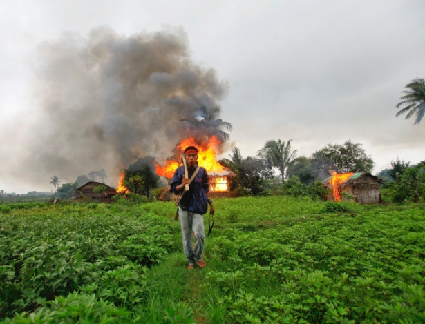 Homem da etnia Rakhine caminha com arma feita manualmente em frente a residências em chamas - Reuters