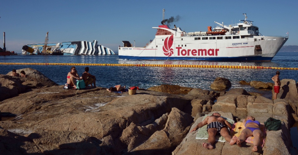 23.jun.2012 - Pessoas tomam sol neste sábado (23) enquanto equipes tentam resgatar o navio Costa Concordia, que naufragou em janeiros deste ano na ilha de Giglio, na Itália