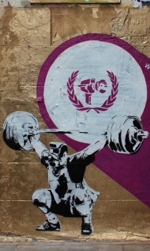 O britânico Codefc tem como marca registrada criar imagens de pessoas com câmeras no lugar de suas cabeças. Ele disse à BBC Brasil que a ideia de criar essa ''assinatura'' foi influenciada por seu trabalho como VJ, que antecedeu sua produção como grafiteiro. A obra aqui mostrada, que fica em Fashion St, no leste da cidade, integra uma série com temas que aludem aos Jogos de Londres 2012 (27/6/12) - #Codefc