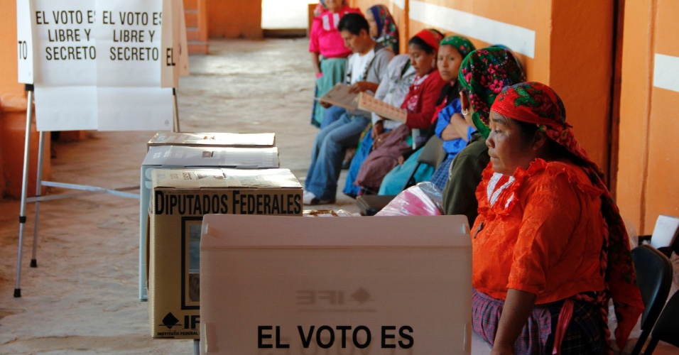 1.jul.2012 - Mulheres esperam em centro de votação perto de avisos onde está escrito "o voto é secreto e livre" em San Bartolome Quialana, na periferia de Oaxaca. Cerca de 80 milhões de mexicanos devem votar neste domingo em 143 mil colégios eleitorais  