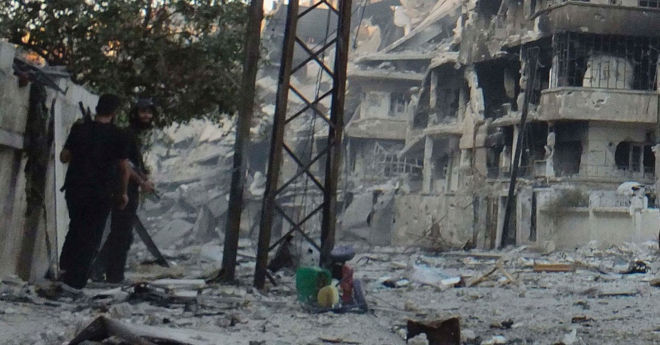 8.jul.2012 - Dois membros do Exército Livre da Síria caminham por bairro destruído por forças do governo em Homs