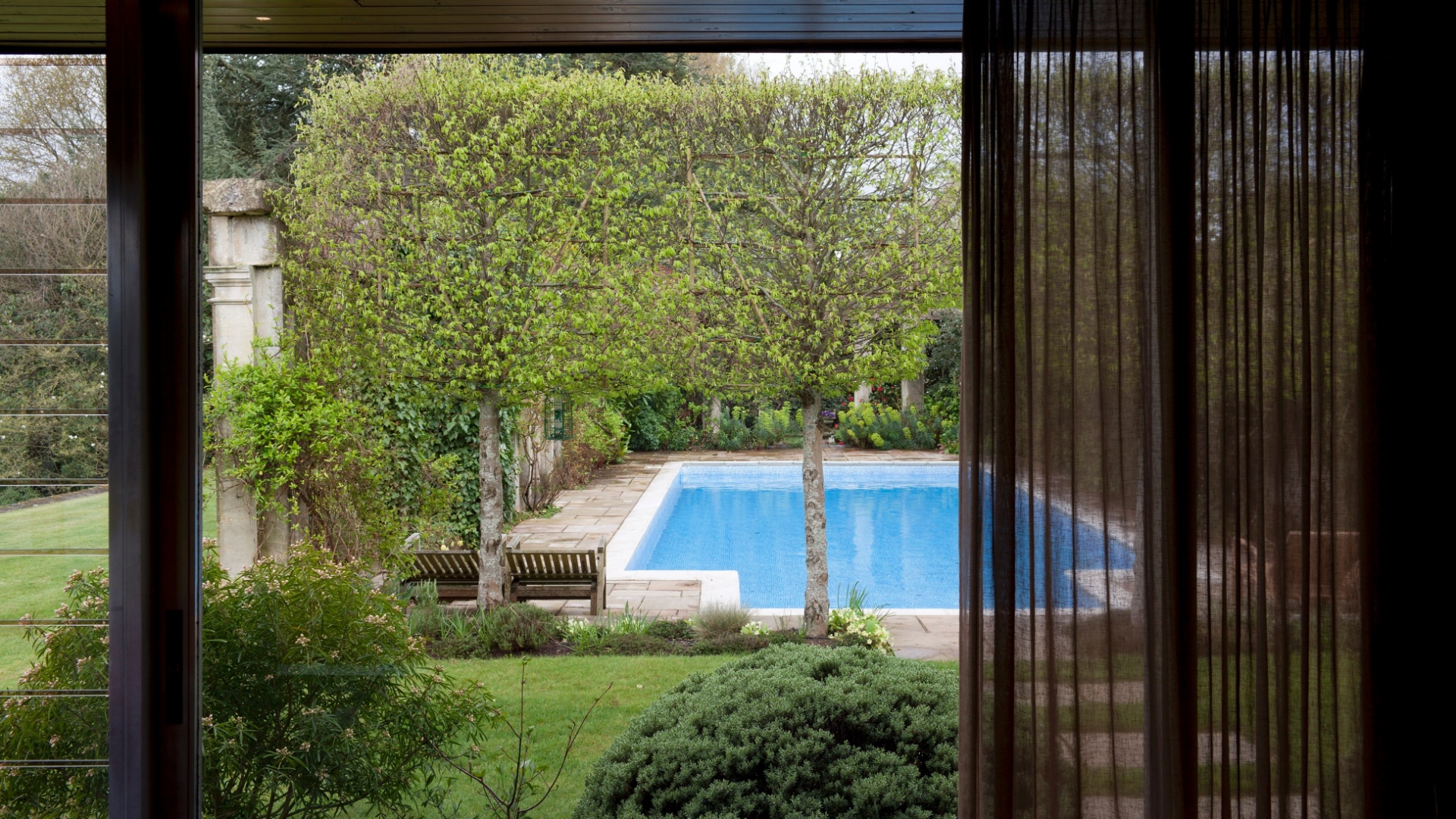 Vista para piscina no quarto do casal na casa de campo de Remy Blumenfeld e seu parceiro Henryk Hetflaisz em Horsmonden, na Inglaterra.  A residência de estilo modernista foi projetada pelo arquiteto britânico Michael Manser em 1969, em uma área de 23 acres - Andreas Meichsner/ The New York Times