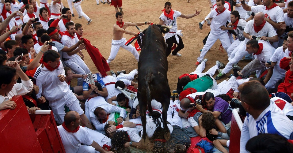 12.jul.2012 - Vaca pula sobre um montinho de foliões em comemoração na arena de Pamplona, no sexto dia do Festival de São Firmino, na Espanha