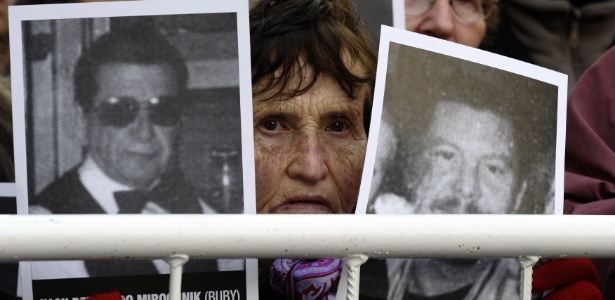 Mulher segura cartazes com retratos de vítimas do bombardeio terrorista contra a Amia - Alejandro Pagni/AFP