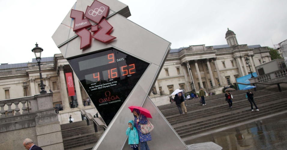 Sob chuva, visitantes posam ao lado do cronômetro que faz a contagem regressiva para a abertura dos Jogos de Londres na Trafalgar Square, praça da capital britânica (18/07/2012)