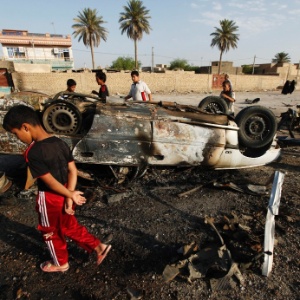 Pessoas observam carro-bomba que explodiu em Mahmudiya, ao sul de Bagdá, no Iraque