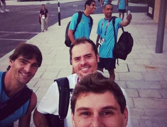 Bruninho, levantador da equipe masculina de Vôlei, tira foto dentro da Vila Olímpica, junto com Giba e Ricardinho; ao fundo, vemos Wallace e Serginho