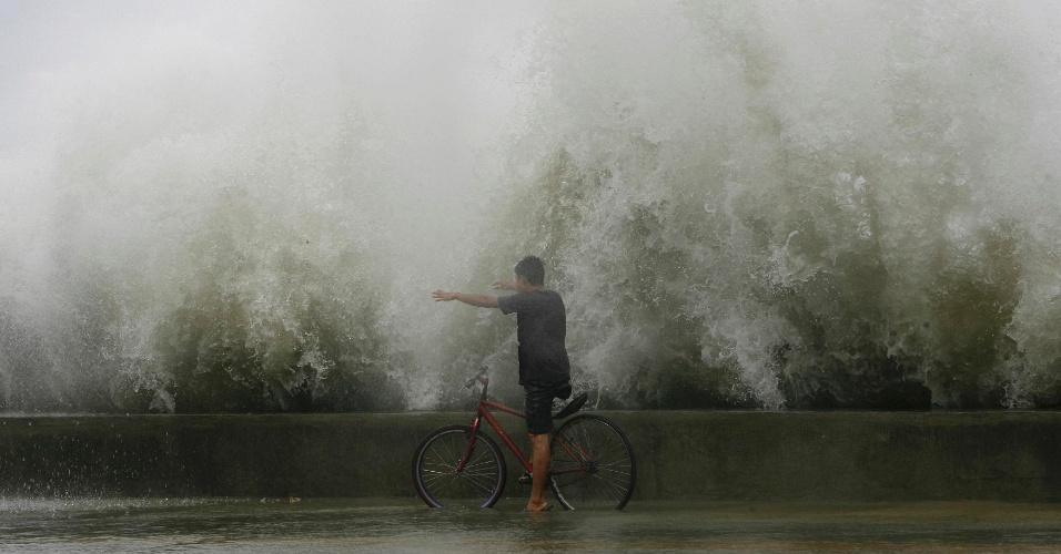 01.ago.2012 -  Homem com sua bicicleta enfrenta as ondas na baía de Manila, provocadas pelo tufão Saola, em uma rua inundada na Roxas Boulevard, nas Filipinas