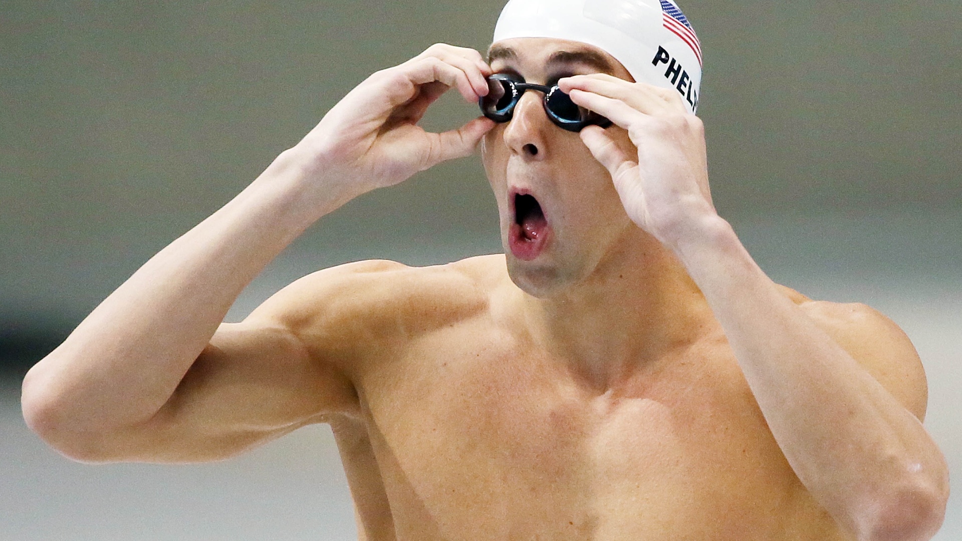 Michael Phelps faz careta enquanto ajeita seus óculos para eliminatória dos 100 m borboleta