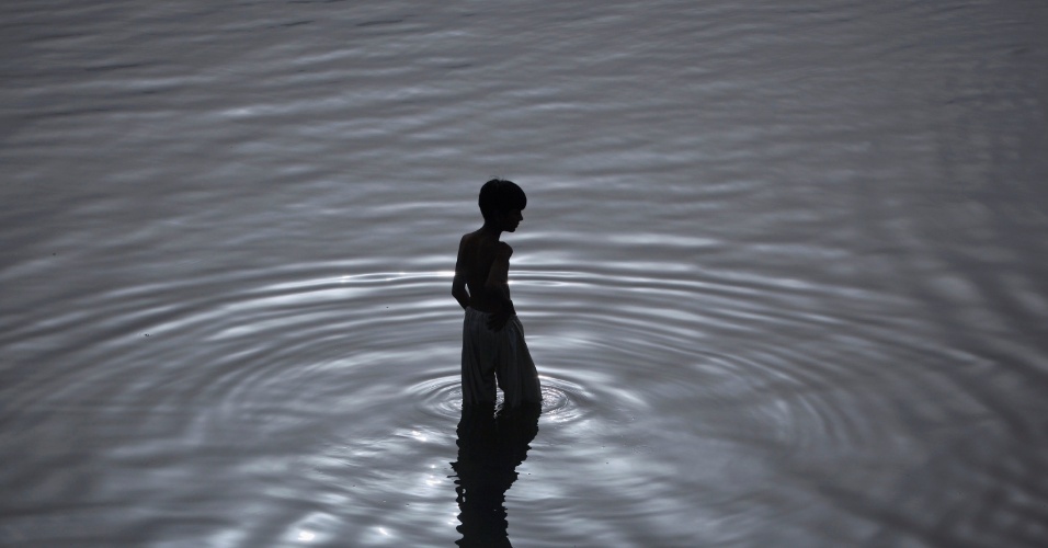 06.ago.2012 -Fotografia mostra a silhueta de um menino caminhando nas águas de um rio no amanhecer, em Karachi, no Paquistão