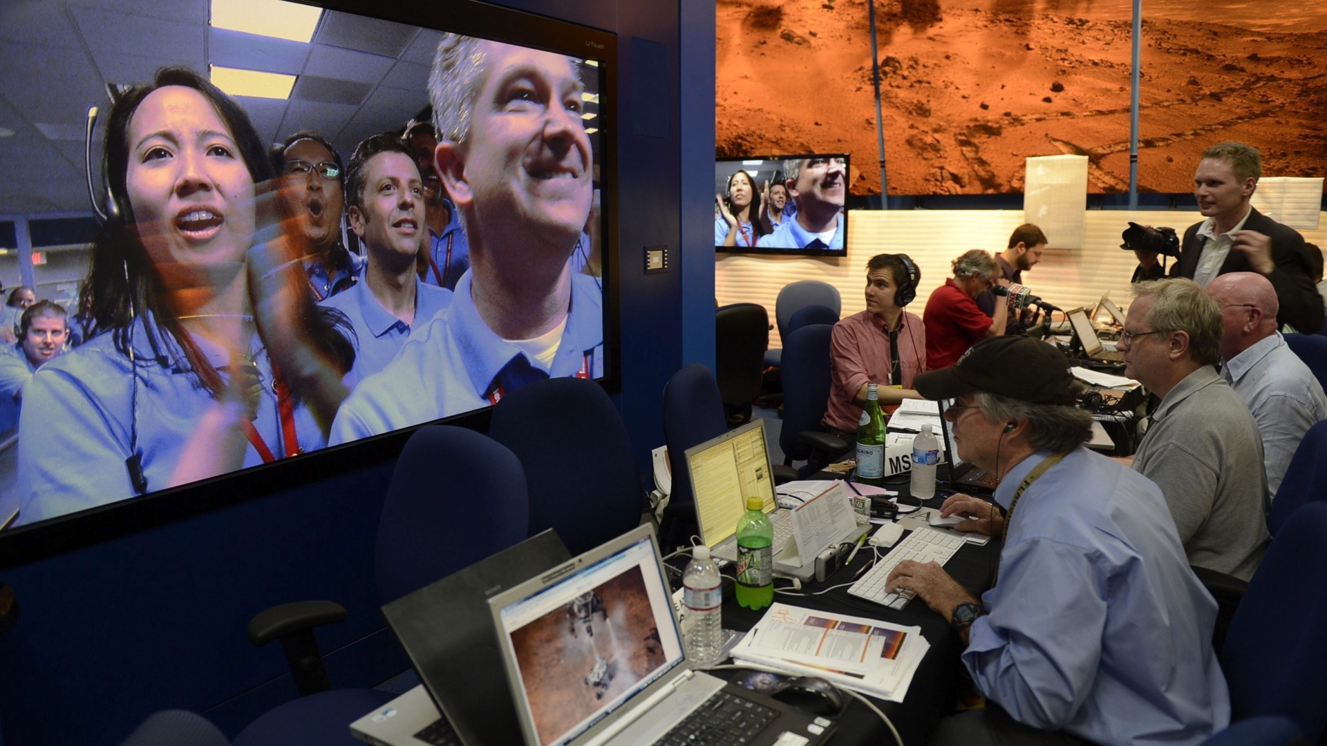 6.ago.2012 - Trabalhadores do laboratório da Nasa (agência espacial americana) comemoram o pouso do robô Curiosity em uma cratera de Marte. A descida pela atmosfera do planeta foi chamada de "sete minutos de terror" por conta das manobras de alto risco que reduziram a velocidade da nave de 20 mil km/h para apenas 1m/s, o que permitiu que as rodas do jipe-robô tocassem a superfície da cratera suavemente - Michael Nelson/EFE