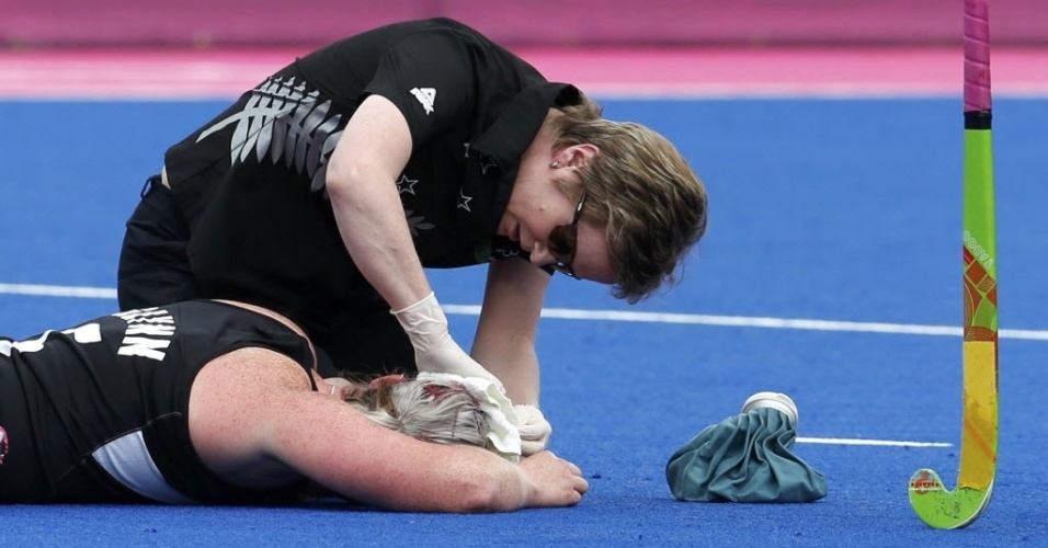 Katie Glynn, da Nova Zelândia, sangra após ser atingida na cabeça na semifinal feminina do hóquei na grama contra a Holanda e é atendida em campo