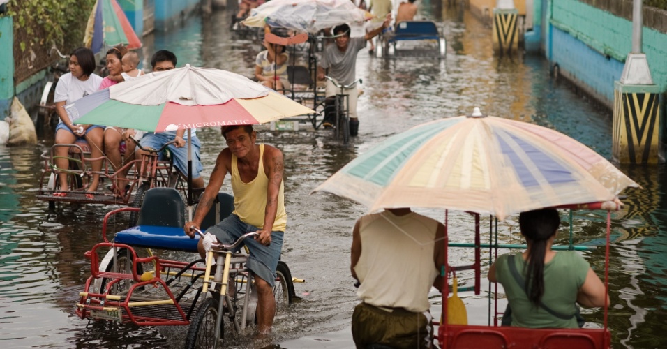 13.ago.2012 - Utilizando bicicletas que funcionam como táxi, pessoas atravessam rua em Valenzuela, bairro do subúrbio de Manila, capital das Filipinas, nesta segunda-feira (13)
