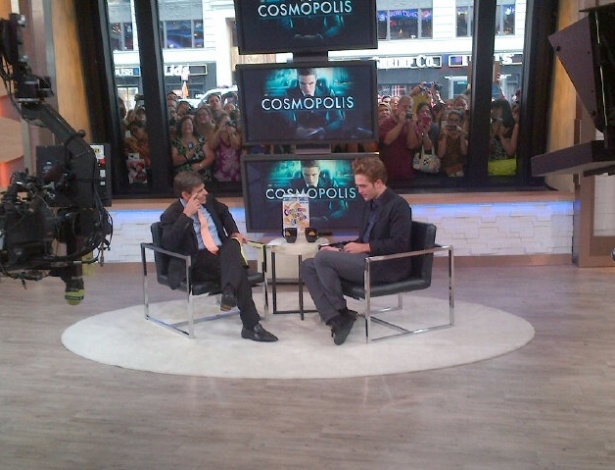 George Stephanopoulos entrevista Robert Pattinson no programa da TV aberta "Good Morning América", enquanto centenas de fãs de aglomeram no vidro que separa o estúdio da calçada em Nova York (15/8/12)