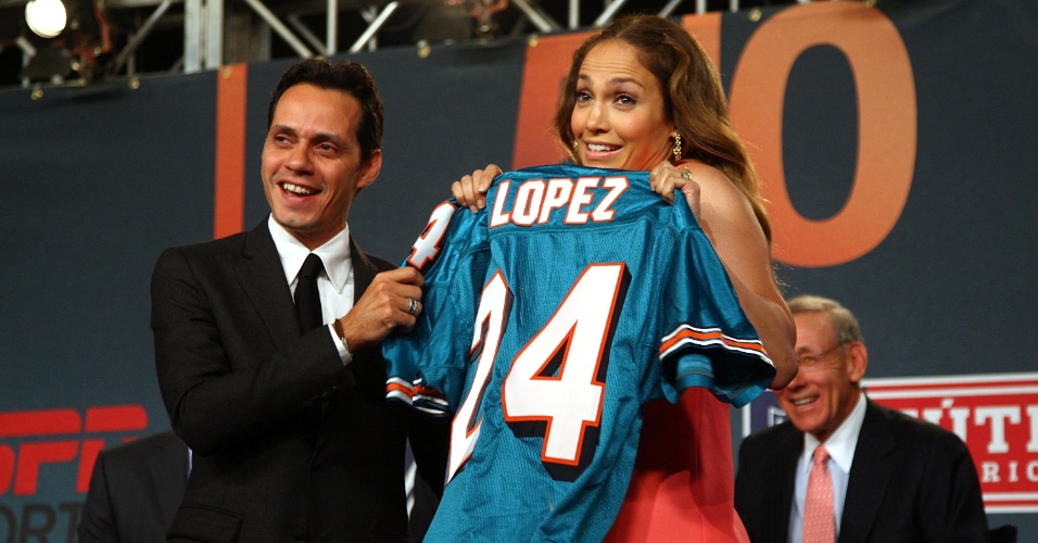Cantores Marc Anthony (e) e Jennifer Lopez mostram camisa do Miami Dolphins, clube de futebol americano do qual são sócios