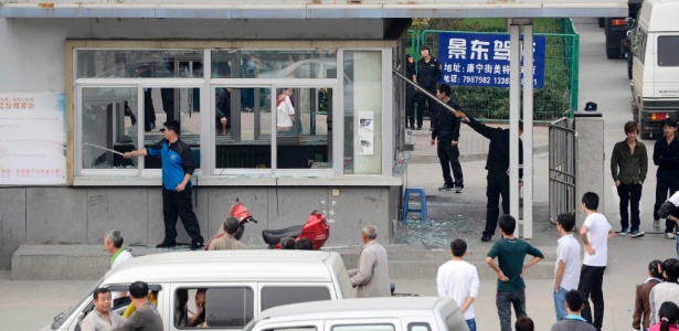 Funcionários retiram vidros quebrados das janelas de uma entrada da fábrica da Foxconn diante de carros da polícia paramilitar chinesa. Cerca de 2.000 funcionários se envolveram em um tumulto generalizado - Reuters