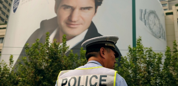 Policial postado em frente a pôster de Federer, que recebeu ameaça de morte na China - AFP PHOTO/Peter PARKS