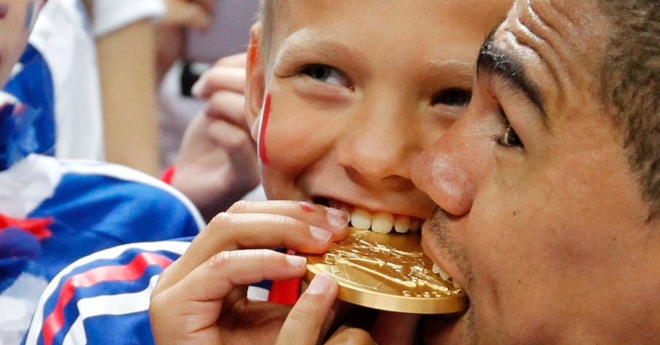 Francês Daniel Narcisse morde a medalha de ouro com o filho Noa após ser campeão do handebol masculino na Olimpíada de Londres (12/08/2012)
