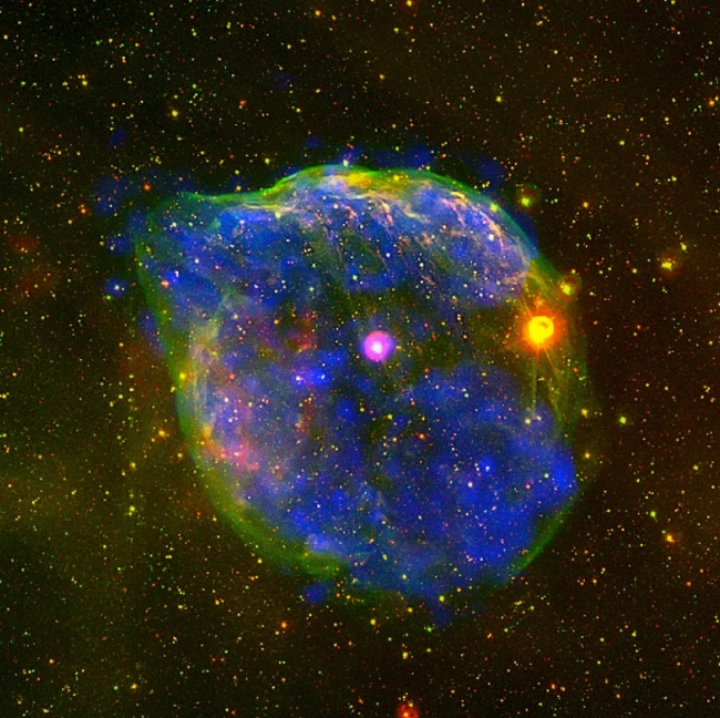 29.out.2012 - A Agência Espacial Europeia (ESA, na sigla em inglês) captou imagens novas - e fantasmagóricas - de uma gigante bolha cósmica a 5.000 anos luz de distância da Terra, na Constelação Cão Maior. Com cerca de 60 anos-luz de diâmetro, o objeto foi formado pelo forte vento soprado de uma estrela massiva, a Wolf-Rayet HD 50896 (ponto rosa no centro). Visíveis apenas em raio X, as marcas azuis representam o plasma quente do sopro estelar e o halo verde surge do choque entre o material ejetado pela estrela e as camadas de gás e poeira no espaço