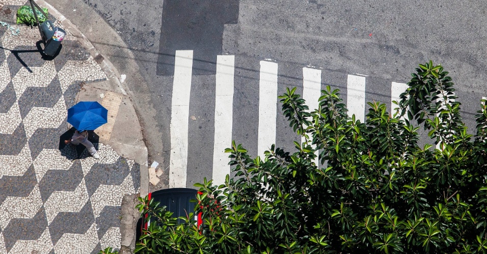 29.out.2012 - Pedestre se protege do sol e calor de mais de 30°C no bairro da Bela Vista, no centro de São Paulo