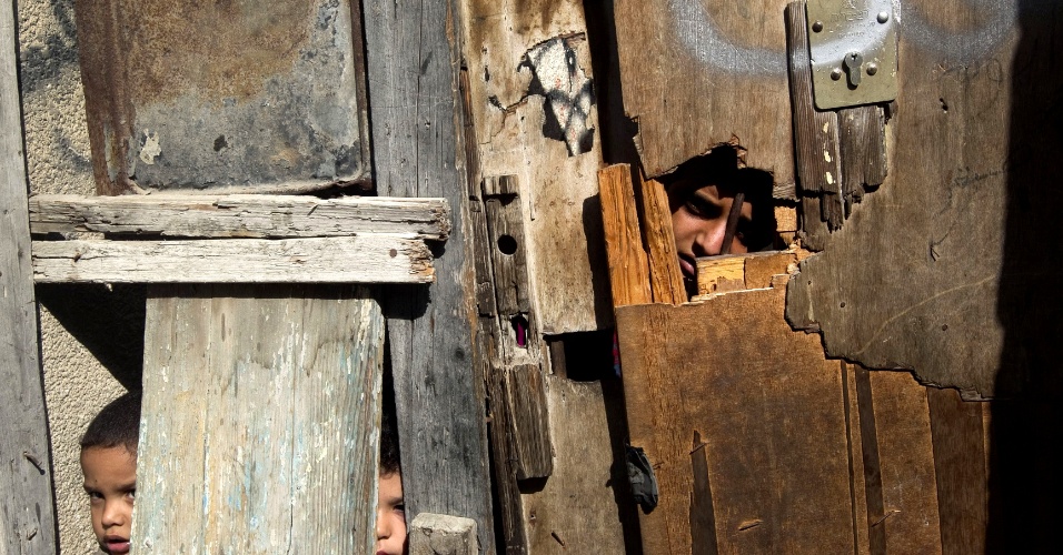 3.nov.2012 - Crianças palestinas observam através de frestas em uma porta de madeira no campo de refugiados de Shati, na Cidade de Gaza. Autoridades palestinas demandam de Israel o direito de retorno a casa, dos refugiados, o que é negado. Israel afirma que eles devem ser acomodados dentro de um Estado palestino