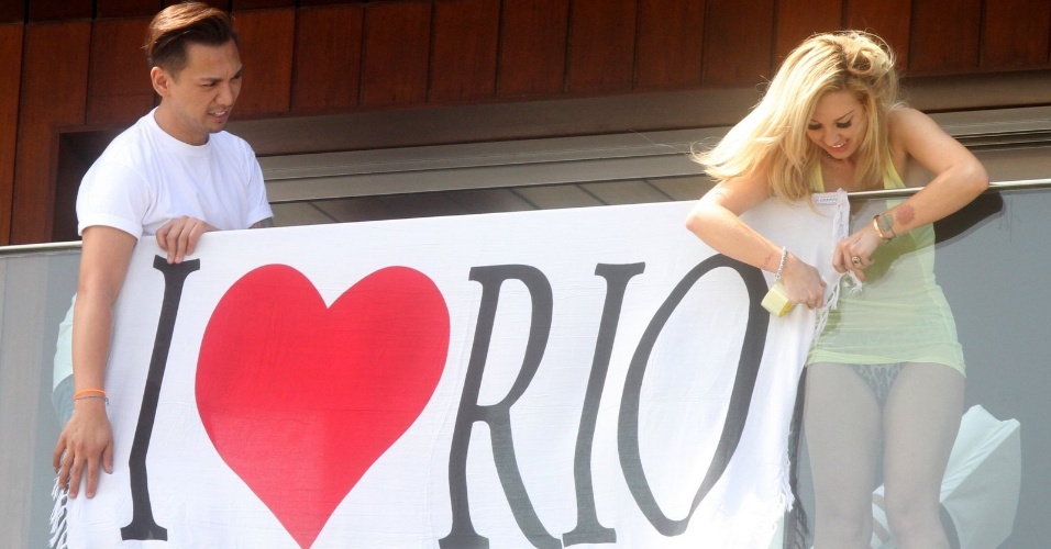 Maquiadora de Lady Gaga (à dir.), Tara Savelo, estende bandeira em que se lê "Eu amo o Rio" na sacada do hotel do Rio de Janeiro (7/11/12)