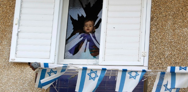Criança israelense observa janela estilhaçada por um foguete supostamente disparado por militantes palestinos da Faixa de Gaza, nesta segunda-feira (12), em Netivot. Ninguém ficou ferido 