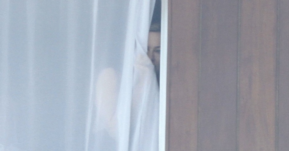 1.dez.2012 - Madonna dá uma olhada através da cortina de seu quarto de hotel, após ouvir rojões soltador por fãs