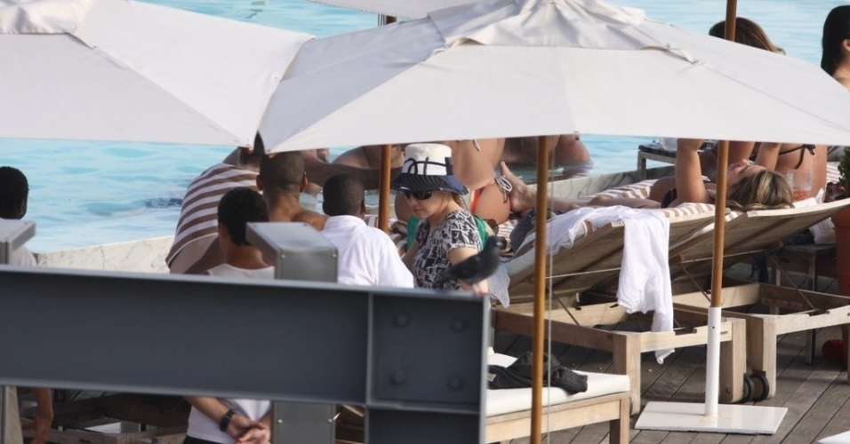 1.dez.2012: De chapéu e manga comprida, Madonna se protege debaixo do guarda-sol em piscina do hotel. A cantora apresenta domingo (2) no Rio de Janeiro
