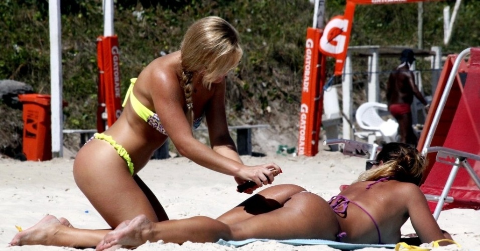 18.dez.2012 - Thaiz Schmitt, coelhinha da "Playboy" passa bronzeador em Caren Souza, apresentadora do programa "Malícia", curtiram a praia da Barra, zona oeste do Rio