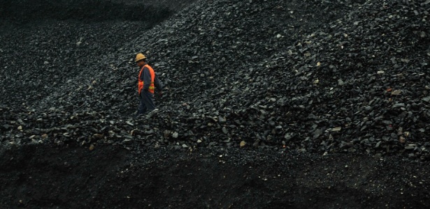 Trabalhador anda entre as pilhas de carvão de uma carvoaria na China. Segundo relatório da agência Internacional de Energia, o carvão será primeira fonte de energia mundial em dez anos, superando o petróleo, devido ao desenvolvimento acelerado dos países emergentes, como China e Brasil
