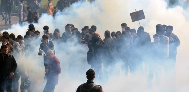 Manifestantes se protegem de gás lacrimogêneo jogado pela polícia durante o protesto