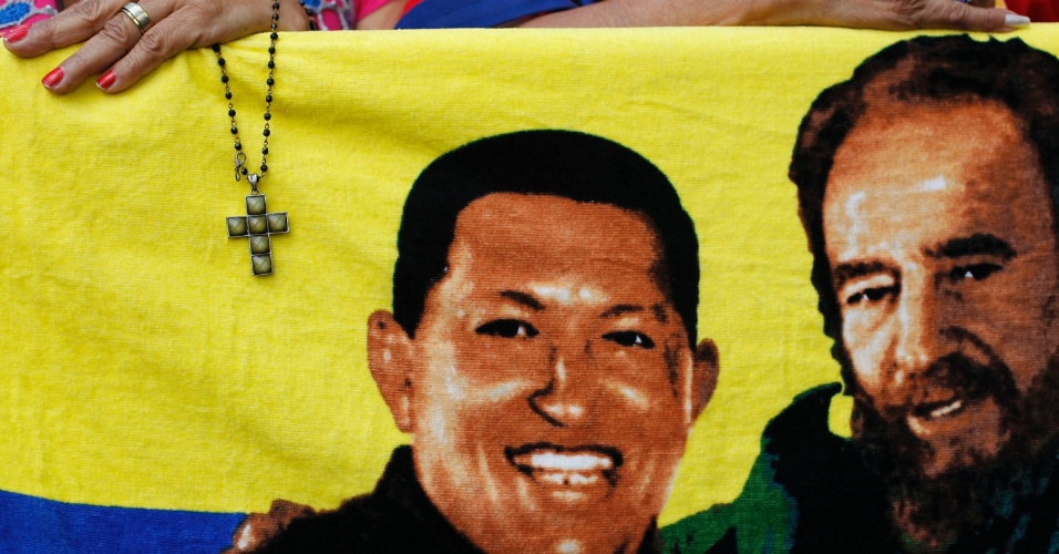 5.jan.2013 - Mulher segura um crucifixo junto de uma imagem de Hugo Chávez ao lado de Fidel Castro, ex-líder cubano. O presidente da Venezuela está hospitalizado em Cuba em estado grave depois de ter sido operado para a retirada de um câncer