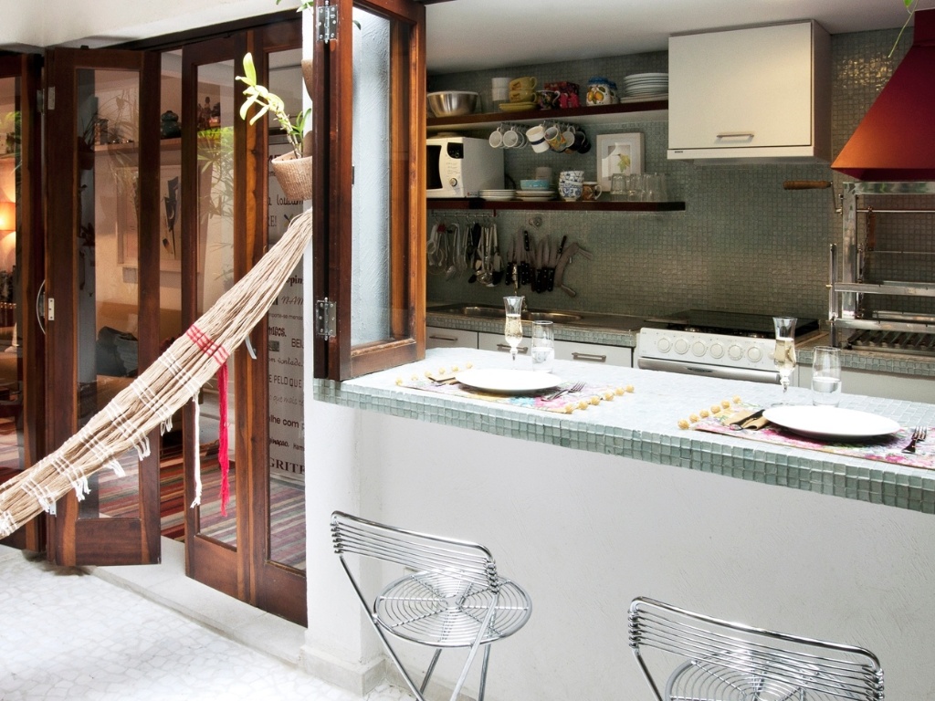 O canto para refeições que se divide entre a cozinha e a varanda foi criado pela arquiteta Crisa Santos com a abertura de uma janela do tipo camarão sobre o balcão revestido com as mesmas pastilhas (Vidrotil) adotadas na parede da cozinha. Para o conforto dos comensais a arquiteta optou pelas banquetas aramadas (Spicy) - Lucas Fonseca/ Divulgação