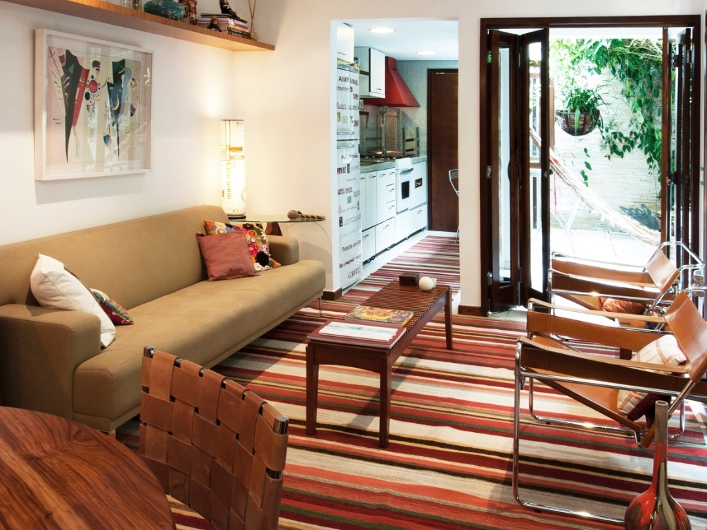 No projeto da arquiteta Crisa Santos, a cozinha (7,5 m²) funciona como ponto de interseção entre a sala (17 m²) e a varanda. Os eletrodomésticos e armários estão dispostos em uma das paredes, liberando a oposta para o balcão de refeições. Perceba que para integrar a cozinha com o estar, além optar por um vão sem porta, a arquiteta usou o tapete (Gaia) dando unidade aos ambientes - Lucas Fonseca/ Divulgação