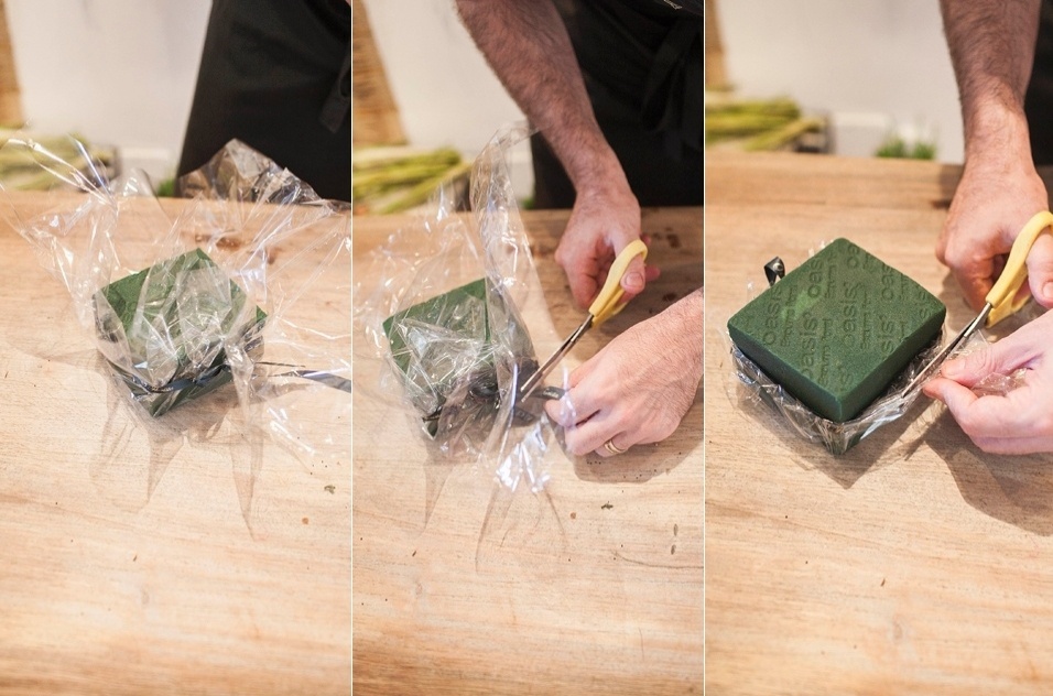 Neste exemplo de arranjo, o papel celofane vai encapar a base da espuma floral, funcionando assim como uma epécie de recipiente. Coloque a espuma no centro de uma folha de celofane e amarre-o com a fita mais ou menos na metade da altura da base porosa. Em seguida, recorte as rebarbas do celofane - Leonardo Soares de Souza/ UOL