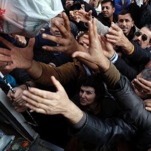 População se espreme para pegar frutas e vegetais distribuídos gratuitamente por agricultores durante protesto contra os preços altos em frente ao ministério da Agricultura, em Atenas, na Grécia